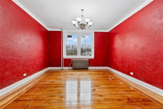 empty room with ornamental molding, radiator heating unit, wood-type flooring, and an inviting chandelier