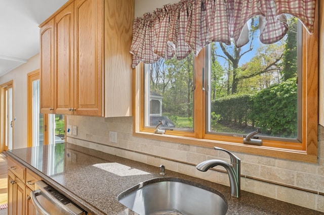 kitchen featuring dark stone countertops, stainless steel dishwasher, decorative backsplash, and a sink