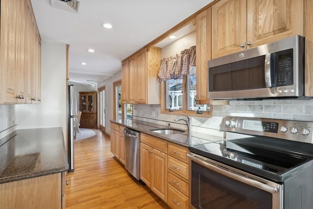 kitchen with dark stone countertops, a sink, stainless steel appliances, light wood-type flooring, and visible vents