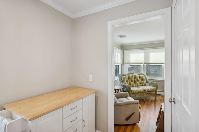 sitting room with ornamental molding, baseboard heating, visible vents, and wood finished floors