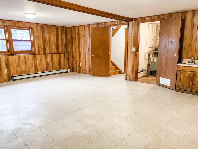 empty room featuring beamed ceiling, sink, baseboard heating, and wood walls