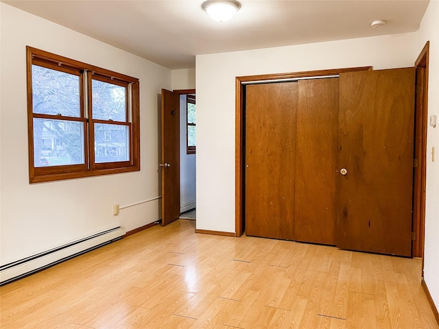 unfurnished bedroom with light hardwood / wood-style flooring, baseboard heating, and a closet