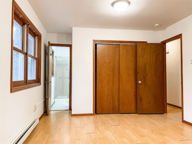 unfurnished bedroom with a baseboard heating unit, light wood-type flooring, and a closet