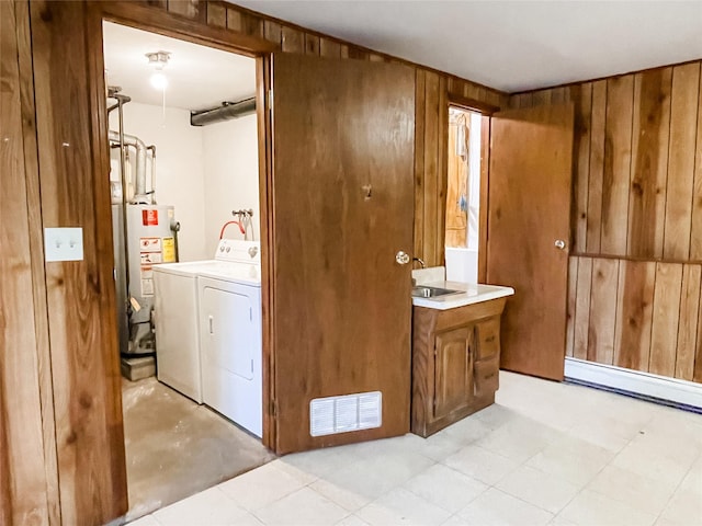 clothes washing area with a baseboard radiator, water heater, wood walls, and washing machine and clothes dryer