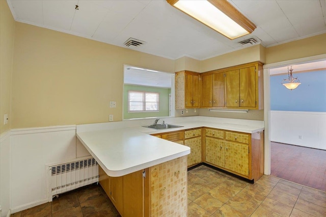 kitchen featuring kitchen peninsula, radiator heating unit, pendant lighting, and sink