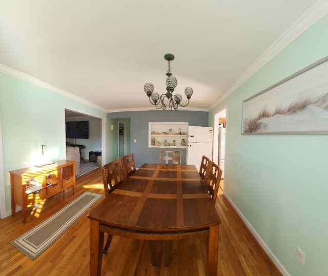 dining area featuring hardwood / wood-style floors, built in shelves, ornamental molding, and a notable chandelier