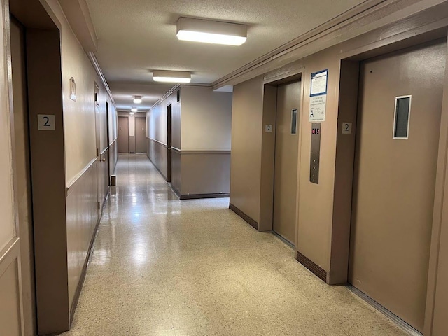 corridor featuring a textured ceiling, elevator, and ornamental molding