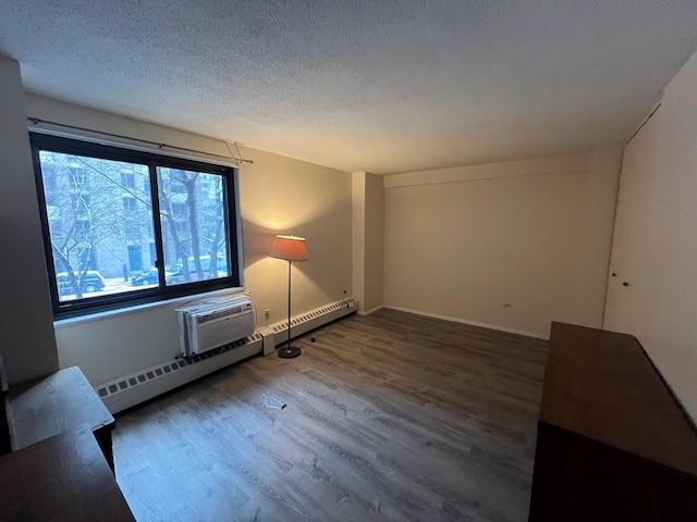 empty room with wood-type flooring, a textured ceiling, an AC wall unit, and baseboard heating