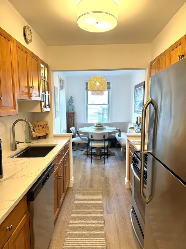 kitchen with brown cabinets, a sink, stainless steel appliances, light wood finished floors, and light stone countertops