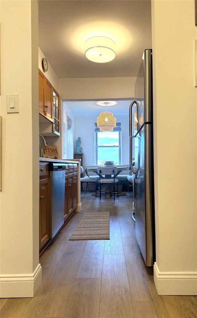 kitchen featuring wood finished floors, brown cabinetry, baseboards, and stainless steel appliances