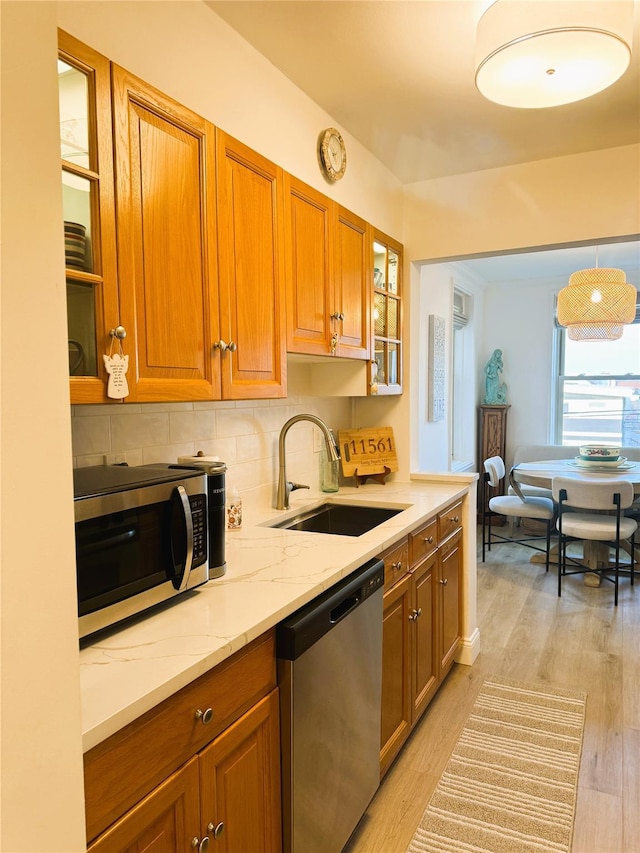 kitchen featuring light stone countertops, light wood-type flooring, brown cabinets, stainless steel appliances, and a sink