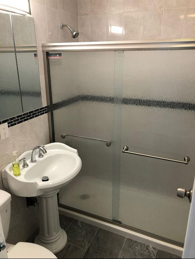 bathroom featuring toilet, a shower with shower door, and tile walls