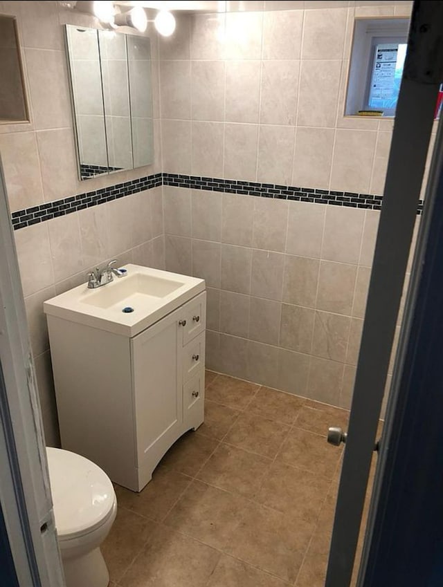 bathroom with toilet, vanity, tile patterned floors, and tile walls