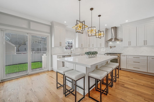 kitchen with white cabinetry, wall chimney exhaust hood, pendant lighting, a breakfast bar area, and appliances with stainless steel finishes