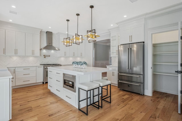 kitchen with a center island, wall chimney range hood, decorative light fixtures, premium appliances, and white cabinetry