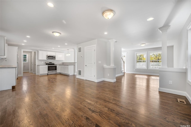 unfurnished living room featuring dark wood-type flooring, visible vents, and ornate columns