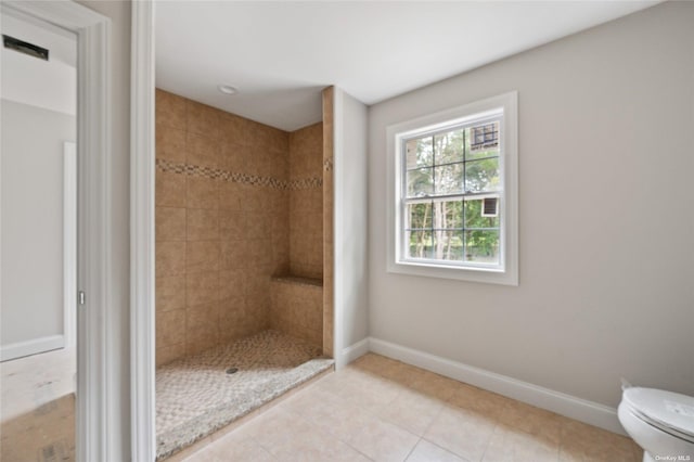 bathroom with a tile shower, toilet, and tile patterned floors