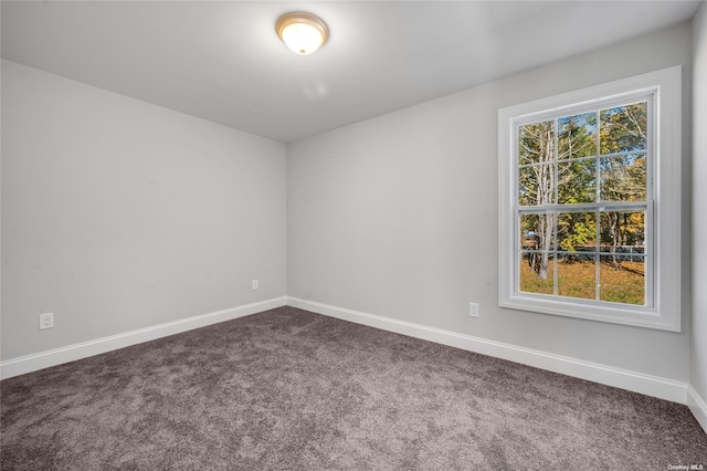 unfurnished room with baseboards, a healthy amount of sunlight, and dark carpet