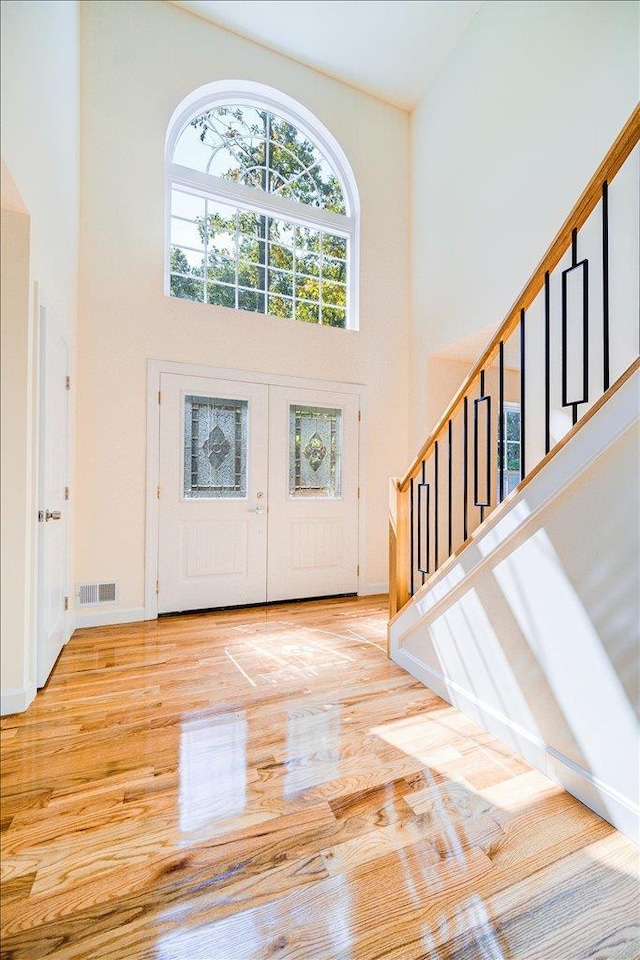 entrance foyer with light hardwood / wood-style floors, a towering ceiling, and french doors