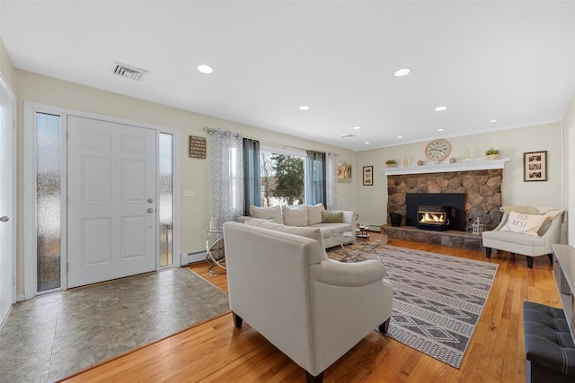 living room featuring baseboard heating, a fireplace, and hardwood / wood-style flooring