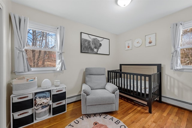 bedroom featuring wood-type flooring, a baseboard heating unit, and a crib