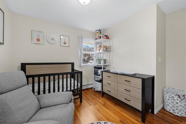 bedroom with baseboard heating, a nursery area, and light hardwood / wood-style floors