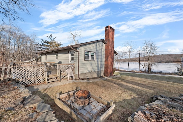 rear view of property featuring a deck with water view and an outdoor fire pit