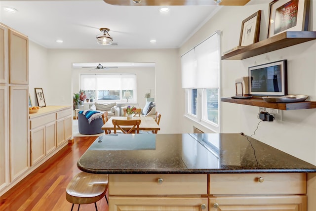 kitchen featuring a breakfast bar, ceiling fan, crown molding, light hardwood / wood-style flooring, and dark stone countertops