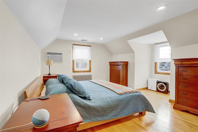 bedroom with radiator heating unit, a wall mounted air conditioner, lofted ceiling, and light hardwood / wood-style flooring