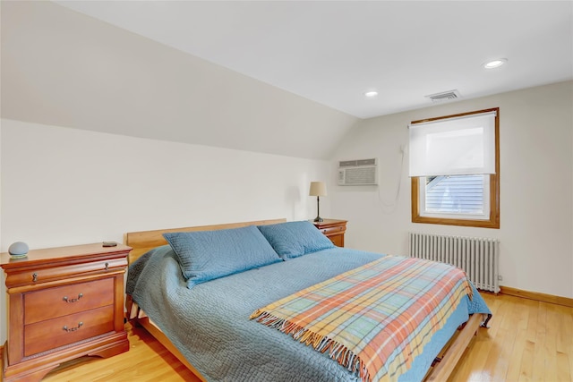 bedroom featuring radiator heating unit, light hardwood / wood-style floors, a wall mounted AC, and lofted ceiling