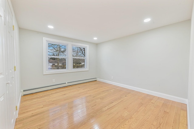 spare room featuring baseboard heating and light hardwood / wood-style flooring