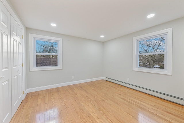 unfurnished room with a wealth of natural light, a baseboard radiator, and light wood-type flooring