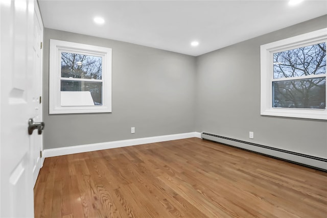 unfurnished room featuring a healthy amount of sunlight, a baseboard heating unit, and light hardwood / wood-style floors