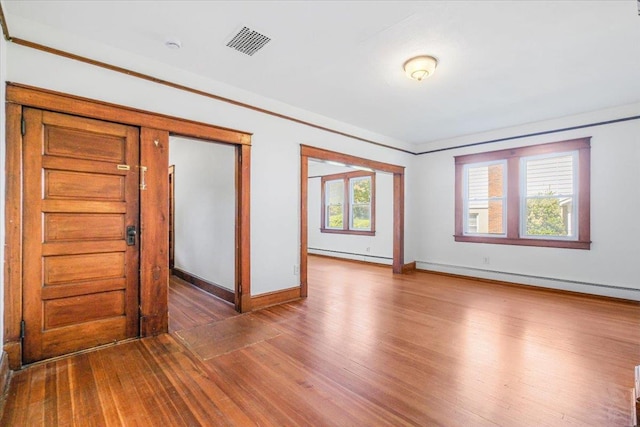 empty room featuring dark hardwood / wood-style floors, baseboard heating, and a healthy amount of sunlight