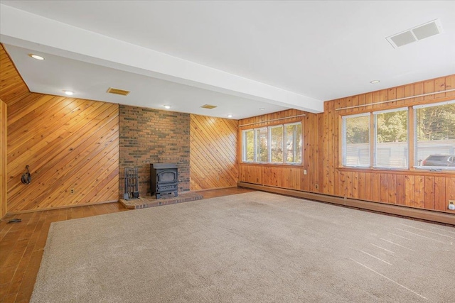 unfurnished living room featuring beam ceiling, a wood stove, wooden walls, and baseboard heating