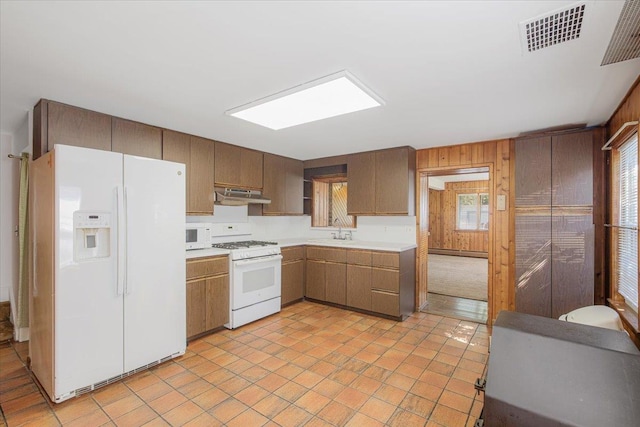 kitchen with white appliances, exhaust hood, wooden walls, light tile patterned floors, and baseboard heating