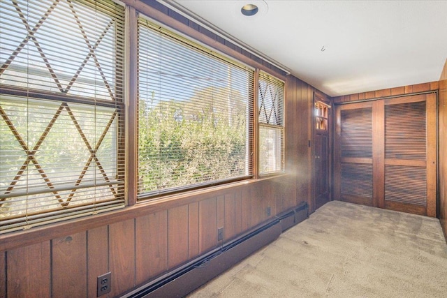 hallway featuring baseboard heating, wooden walls, and light colored carpet