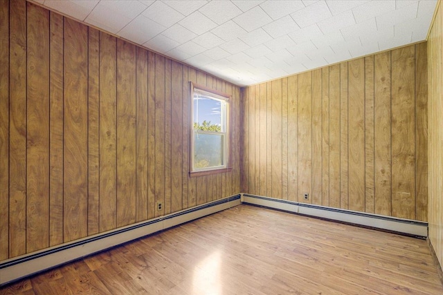 empty room with light hardwood / wood-style floors, baseboard heating, and wooden walls