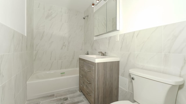 full bathroom featuring tiled shower / bath, vanity, tile walls, and toilet