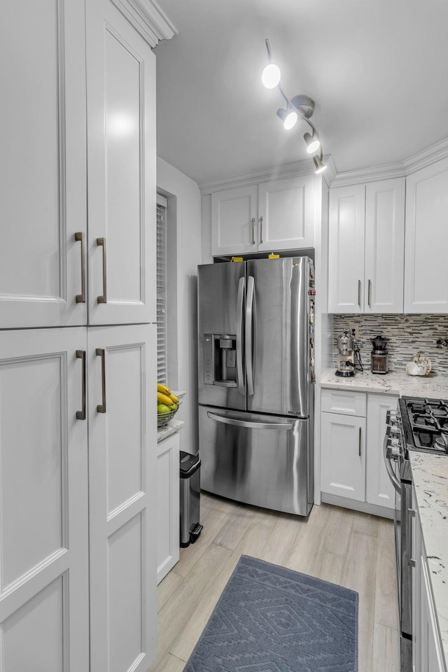 kitchen with appliances with stainless steel finishes, light wood-type flooring, light stone counters, white cabinetry, and tasteful backsplash