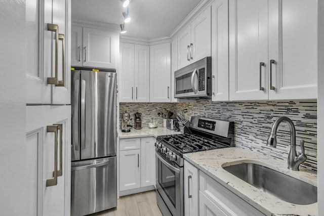 kitchen featuring stainless steel appliances, sink, white cabinetry, light stone counters, and backsplash