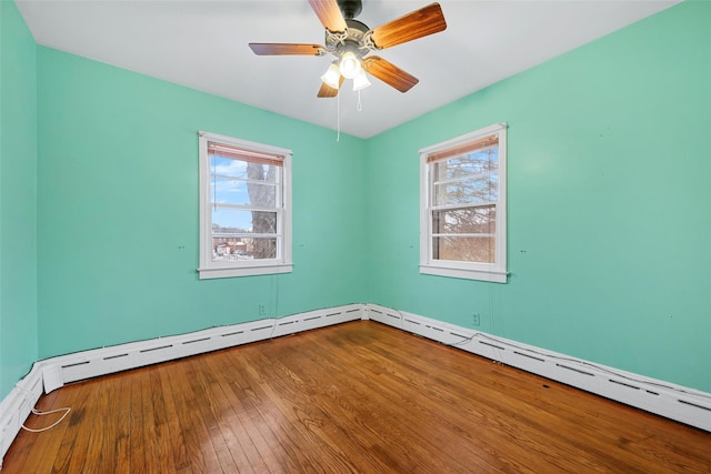 empty room featuring plenty of natural light, hardwood / wood-style floors, ceiling fan, and baseboard heating