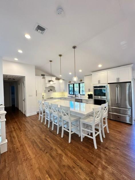 kitchen featuring dark hardwood / wood-style floors, appliances with stainless steel finishes, decorative light fixtures, a kitchen bar, and white cabinetry