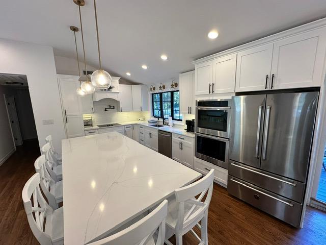 kitchen featuring pendant lighting, light stone countertops, tasteful backsplash, white cabinetry, and stainless steel appliances