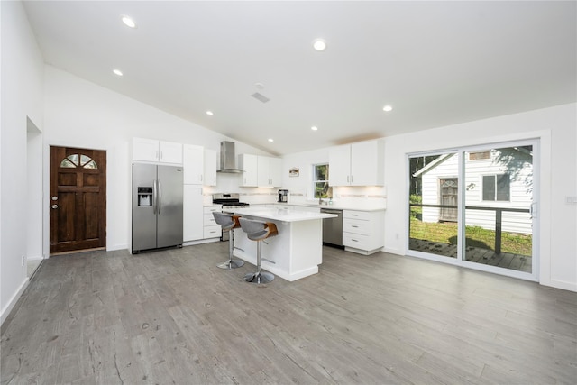 kitchen with appliances with stainless steel finishes, wall chimney range hood, white cabinets, a kitchen island, and a breakfast bar area