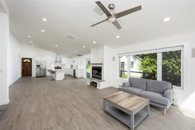 living room featuring a large fireplace, vaulted ceiling, ceiling fan, sink, and light hardwood / wood-style flooring