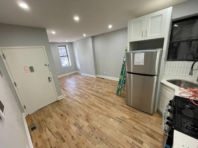 kitchen with black stove, sink, light hardwood / wood-style flooring, white cabinetry, and stainless steel refrigerator