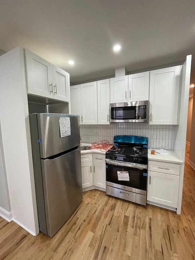 kitchen featuring backsplash, white cabinetry, light wood-type flooring, and appliances with stainless steel finishes