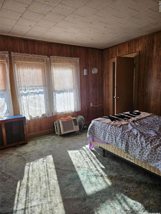 carpeted bedroom featuring wood walls and radiator heating unit