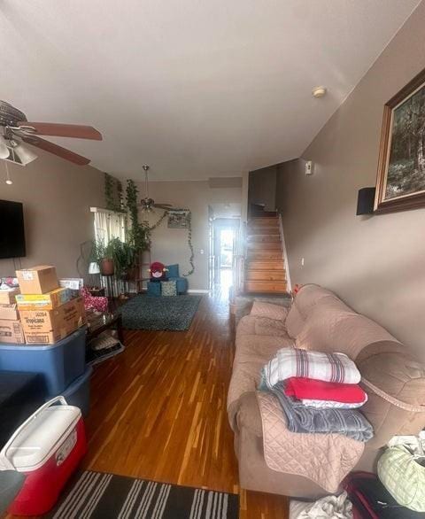 living room with stairs, ceiling fan, and wood finished floors